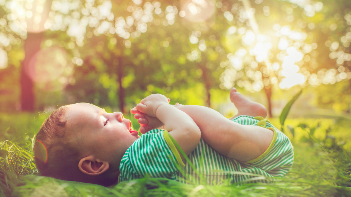 A happy little baby laying on the grass on a sunny day