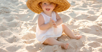 Baby girl in sun hat sitting on beach